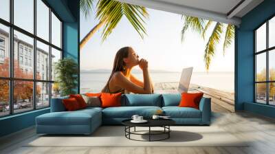 freelancer girl with a computer among tropical palm trees work on the island in sunset Wall mural