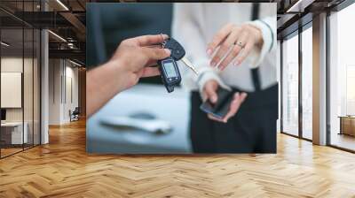 Male hand giving car key to female hand. She is holding a cell p Wall mural