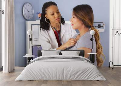 african american doctor listening to heart and lungs of asian patient Wall mural