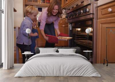 Beautiful white mother using oven mitts to remove cookie tray Wall mural