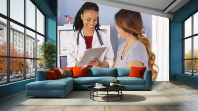 black doctor with tablet talking to female asian patient Wall mural