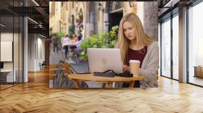 Blonde young lady traveling in Rome checks social media on laptop at local cafe  Wall mural