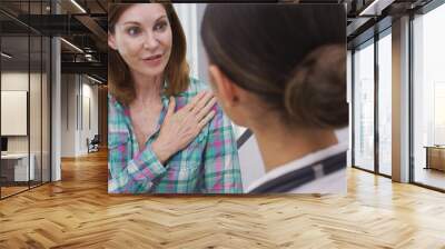 Close up of charming mid aged patient explaining to doctor her uncomfortable shoulder pain. Portrait of senior woman telling young latina doctor about her irritating shoulder joint giving her pain Wall mural