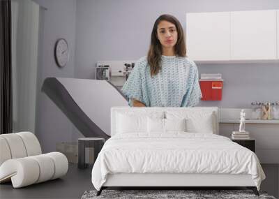 Close up of lovely latina woman seated on medical reclined chair in hospital clinic. Portrait of attractive mixed ethnic patient looking at camera from inside medical clinic wearing somber expression Wall mural