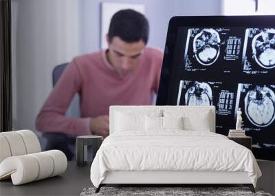 Close up of young hispanic man sitting in medical office waiting for doctor and texting on phone. Close view of patients ct-scans on computer while he uses smartphone to send text messages Wall mural