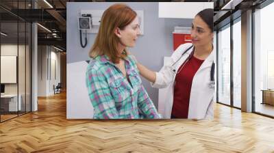 Close up of young latina doctor giving senior patient good news about future health. Portrait of young doctor and mid aged patient talking inside medical clinic  about good health Wall mural