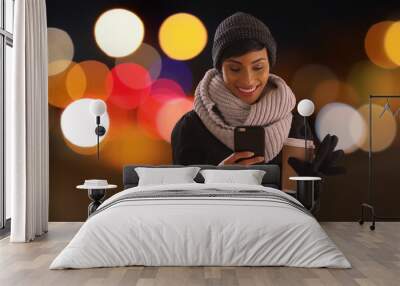 Cute black woman in her 20s texting on phone in urban setting with bokeh lights Wall mural