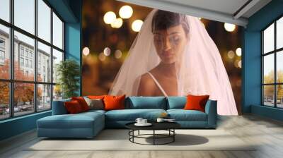 Elegant bride posing outdoors in evening looking down veil covering face softly Wall mural