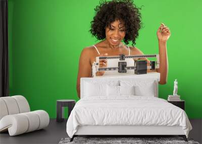 Happy African American woman adjusting weight scale on greenscreen Wall mural