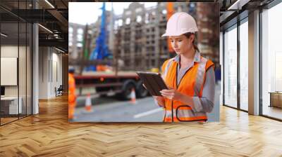 Hardworking Caucasian female construction worker looking over blueprints on pad Wall mural