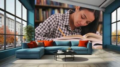 Hardworking Latina student studies for a class in her school library Wall mural