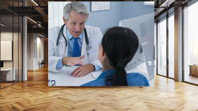 Mature Caucasian male doctor in his office talking to new patient and smiling. Primary care physician explaining medical issue to woman Wall mural