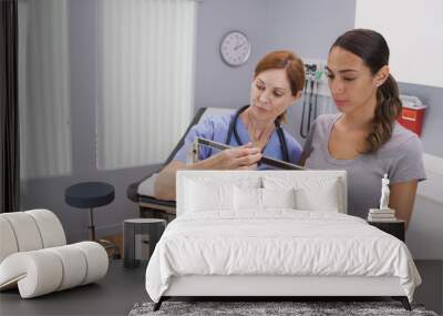 Mid aged caucasian nurse weighing female patient on scale. Charming middle aged nurse using scale to measure weight of young latina patient Wall mural