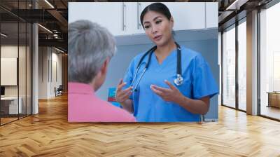 Over the shoulder shot of Japanese woman surgeon going over recovery steps with senior Caucasian man patient in hospital exam room. Nurse or doctor talking to older man Wall mural