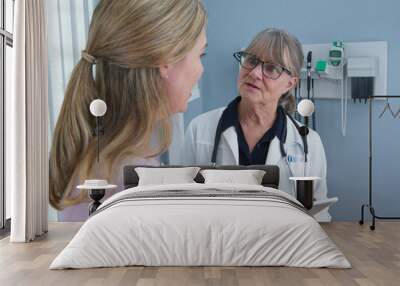 Over the shoulder shot of woman talking to her primary care doctor in exam room. Middle aged patient having appointment with female senior physician Wall mural