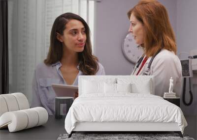 Portrait of lovely young hispanic woman meeting with senior doctor about pregnancy results. Close up of mid aged caucasian doctor using portable tablet to review health history with latina patient Wall mural