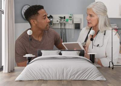 Portrait of young black man consulting with mature female doctor indoors medical clinic. Close up of senior caucasian doctor using tablet computer to share test results with male black patient Wall mural