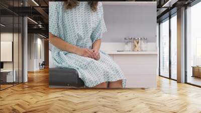 Portrait of young female patient seated on clinic chair wearing hospital gown. Close view of multi ethnic woman sitting on medical seat at hospital clinic Wall mural