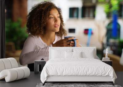 Pretty black woman with curly hair sits outside drinking coffee Wall mural