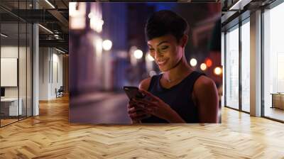 Pretty smiling African American female reads text message on the street at night Wall mural