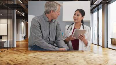 Primary care doctor explaining medical issue to senior male patient in exam room. Female medical professional with tablet computer talking to older man about his health Wall mural