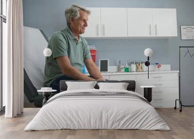 Senior Caucasian male patient waiting patiently for doctor while sitting on exam room table. Older man going to regular appointment for annual check up Wall mural