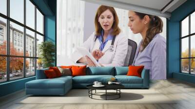 Senior medical physician using tablet computer to share results of patients health condition. Mid aged doctor and young patient looking at high tech tablet indoors medical clinic Wall mural