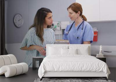 Senior nurse checking health history with young hispanic patient at hospital clinic. Middle aged medical nurse asking patient questions about general health Wall mural