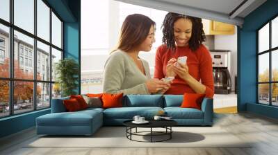 Two close friends using mobile phones and leaning against kitchen counter Wall mural