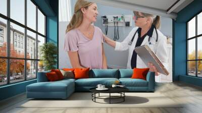 Two shot of woman talking to her reassuring primary care doctor in exam room. Middle aged patient having appointment with female senior physician Wall mural