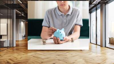 Kid teen boy saving money putting coins in a piggy bank. Learning financial responsibility and projecting savings. The concept of saving money, finance, business and investment, Lessons in mindfulness Wall mural