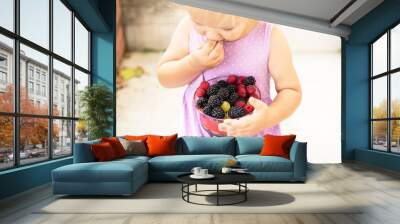 Little cute girl happy to eat fruits - raspberries and blackberries. Toddler holding bawl with fruits outdoors. Yummy and healthy food for kids. Healthy nutrition. Wall mural