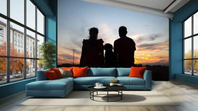 A rear silhouette of a romantic young couple with their dog watching the sunset on the beach Wall mural