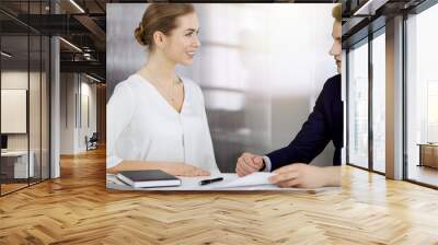 Business people discussing something while sitting in sunny office. Focus at businesswoman while talking to her male colleague Wall mural