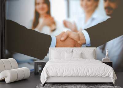 Business people shaking hands at meeting while theirs colleagues clapping and applauding. Group of unknown businessmen and women in modern white office. Success teamwork, partnership and handshake Wall mural