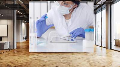 Close-up of professional female scientist in protective eyeglasses making experiment with reagents in laboratory. Medicine and research concept Wall mural