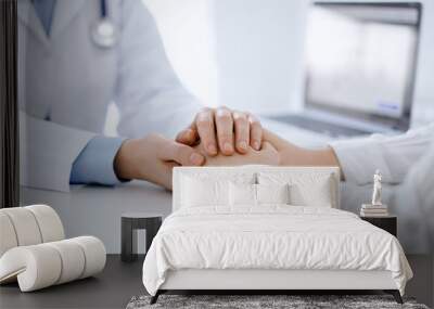 Doctor and patient sitting opposite each other at the table in clinic office. The focus is on female physician's hands reassuring woman, only hands, close up. Medicine concept Wall mural