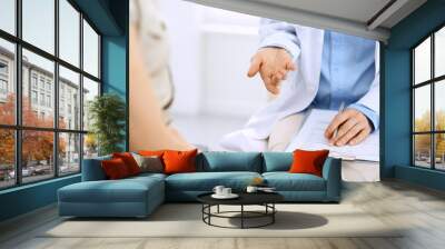 Doctor and patient talking. Physician at work in hospital while writing up medication history records form on clipboard near sitting woman. Healthcare and medicine concepts Wall mural