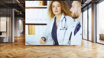 Friendly female doctor sitting in clinic with her male colleague at the background in sunny clinic. Medicine concept Wall mural