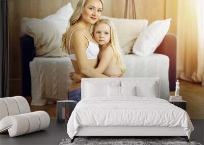 Happy mom and little daughter cuddle while dressing in sunny room. Motherhood and family concept Wall mural