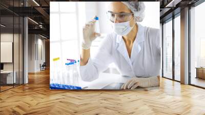 Professional female scientist in protective eyeglasses researching tube with reagents in laboratory. Concepts of medicine and research Wall mural