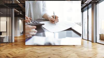 Woman accountant using a calculator and laptop computer while counting and discussing taxes with a client. Business audit concepts Wall mural