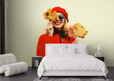 Autumn portrait of happy smiling young woman with yellow maple leaves wearing red french beret on gray background Wall mural