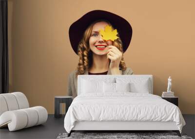 Autumn portrait of stylish happy smiling young woman covering her eyes with yellow maple leaves Wall mural