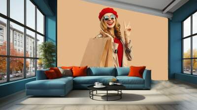 Autumn style outfit, portrait of beautiful happy smiling young woman with shopping bags wearing red french beret hat, gray coat jacket on beige studio background Wall mural