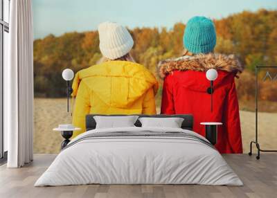 Back view of two young modern women friends standing together on beach, stylish girlfriends on sea Wall mural