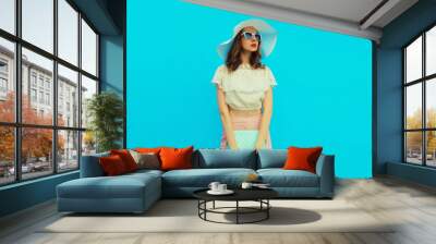 Beautiful caucasian young woman model posing with handbag clutch wearing white summer straw hat on blue studio background Wall mural