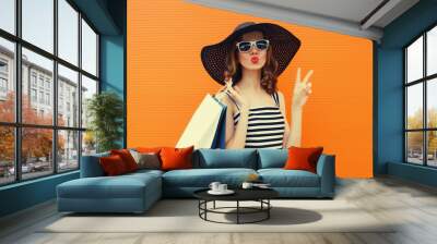 Beautiful happy woman model with shopping bags in summer black hat, dress on orange background Wall mural