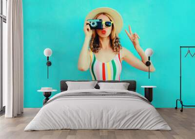 Colorful young woman holding retro camera, blowing red lips sends air kiss in summer straw hat having fun on blue wall background Wall mural