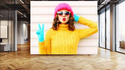 Cooll funny girl blowing red lips wearing colorful knitted yellow sweater pink hat in gloves over white background Wall mural